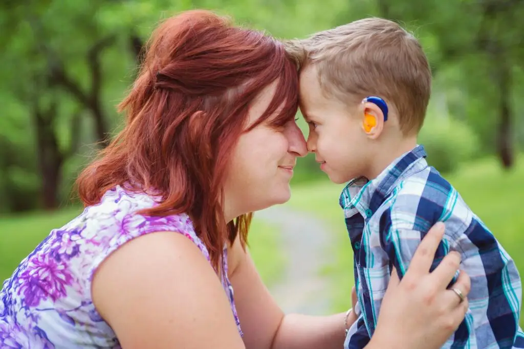 Mother embraces child with hearing aid